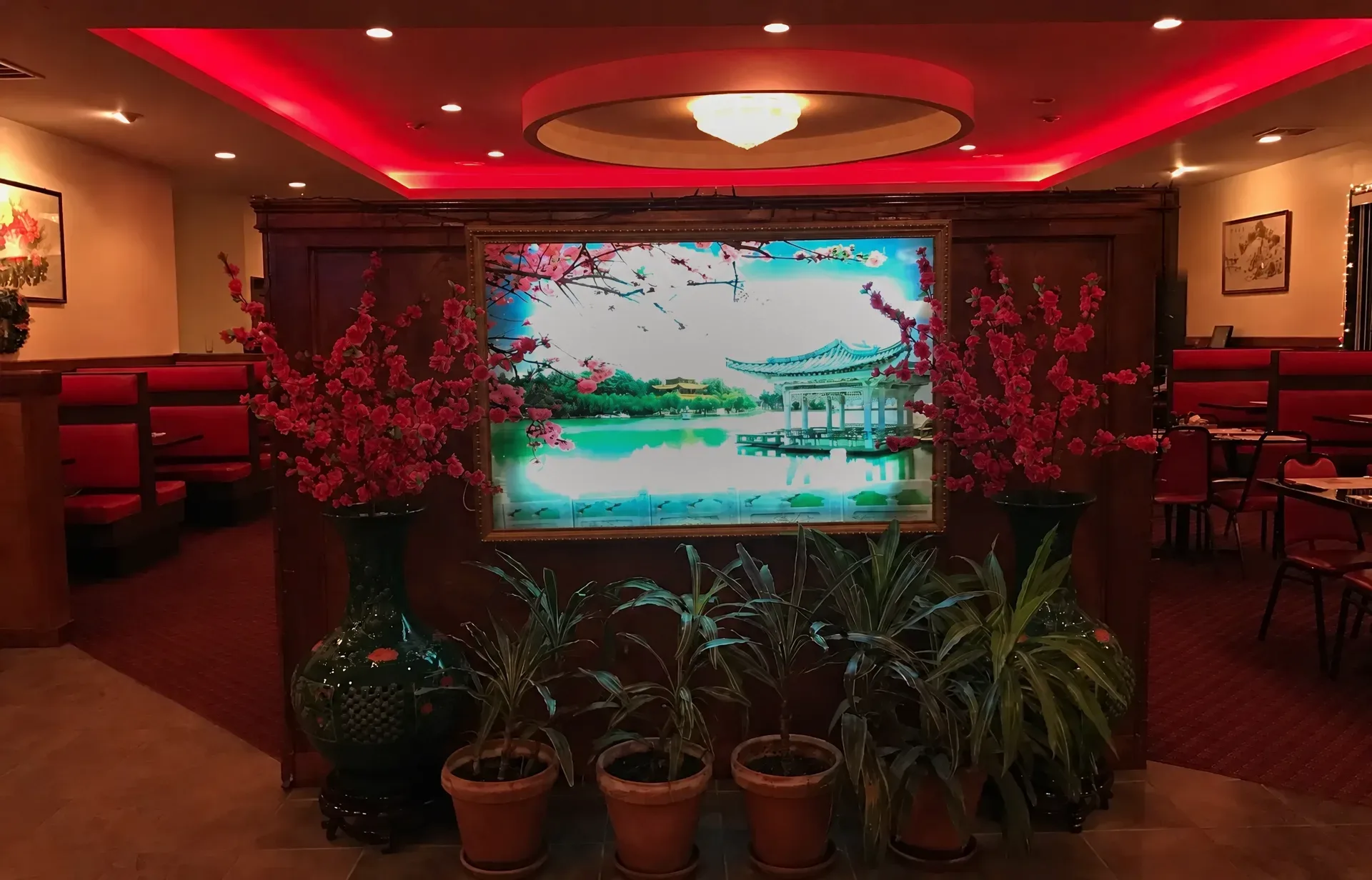 The dining room's carved wood divider with an illuminated lakeside pavilion mural, green vases of pink blossoms and potted plants